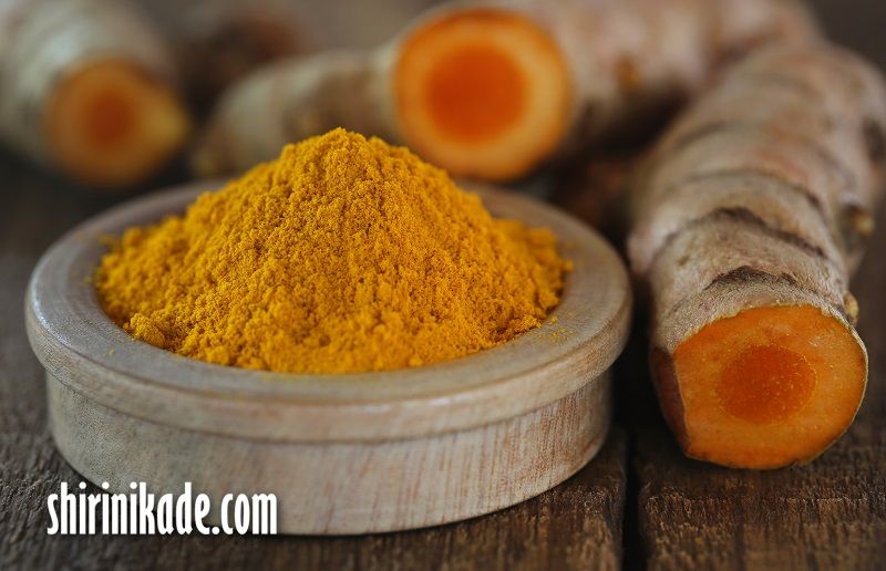 Raw and ground turmeric on wooden surface